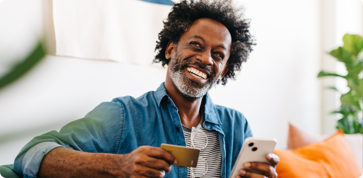 Smiling man sitting on a couch, holding a phone and credit card—representing empowered frontline teams creating confident customer experiences