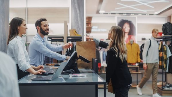 Smiling retail employees helping a customer at checkout, highlighting career visibility’s impact on frontline retention