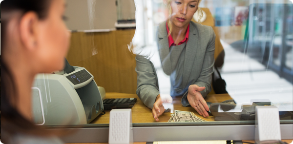 Bank teller counting money behind glass, highlighting urgency of improving branch talent retention in banking