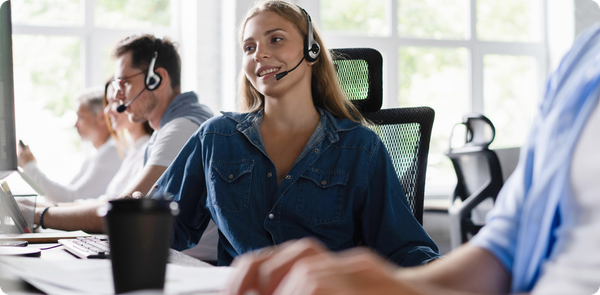 Smiling contact center employee with headset, representing positive coaching and feedback that strengthen frontline performance.