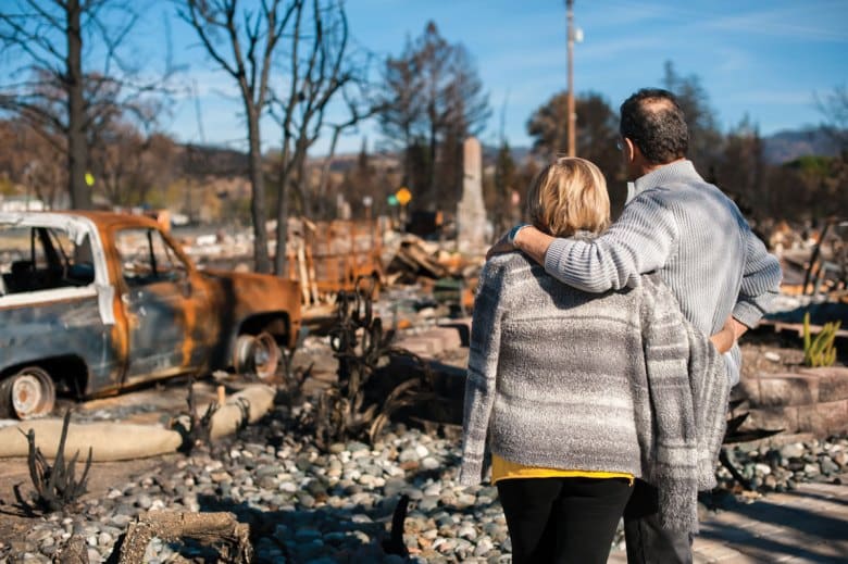 Two people look at the aftermath of a house after a disaster.