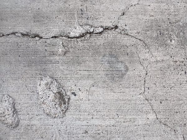 Close-up photograph of cracked concrete surface, showing fine lines and fractures that resemble scars or cuts, symbolising resilience and endurance.