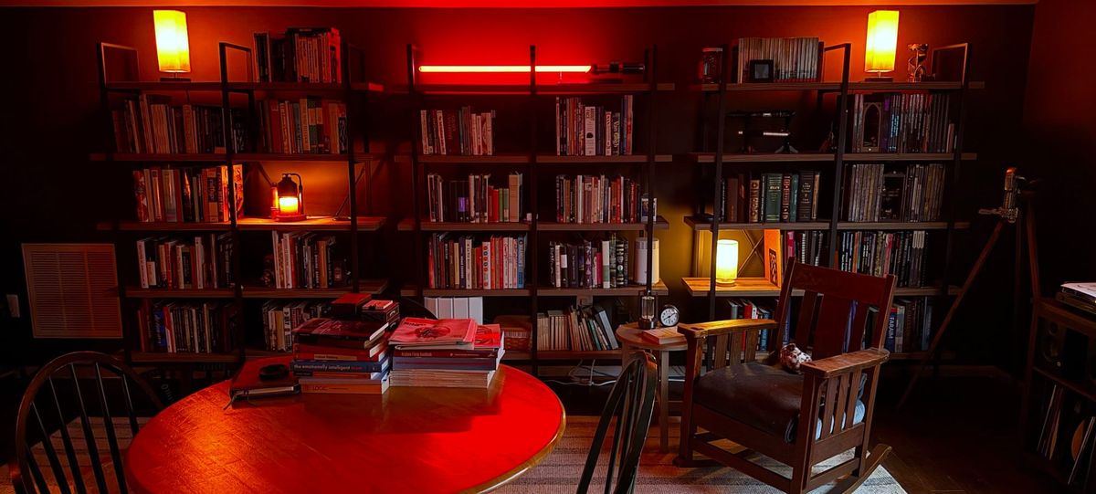 Warm lamps, heavy bookshelves, a work table covered with books, and a cosy rocking chair. An antique wine bottle opener stands in the corner, by the record player.
