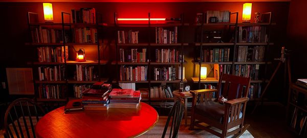 Warm lamps, heavy bookshelves, a work table covered with books, and a cosy rocking chair. An antique wine bottle opener stands in the corner, by the record player.