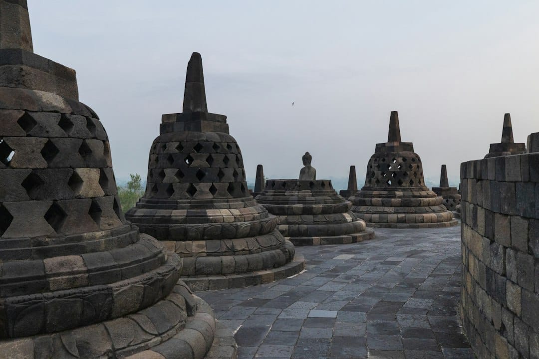 Bell-shaped stupas and a seated Buddha statue on the upper terraces of Borobudur temple