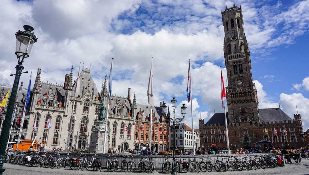The Belfort tower rising over the Markt square in Bruges, with step-gabled guild houses and the neo-Gothic Provincial Court