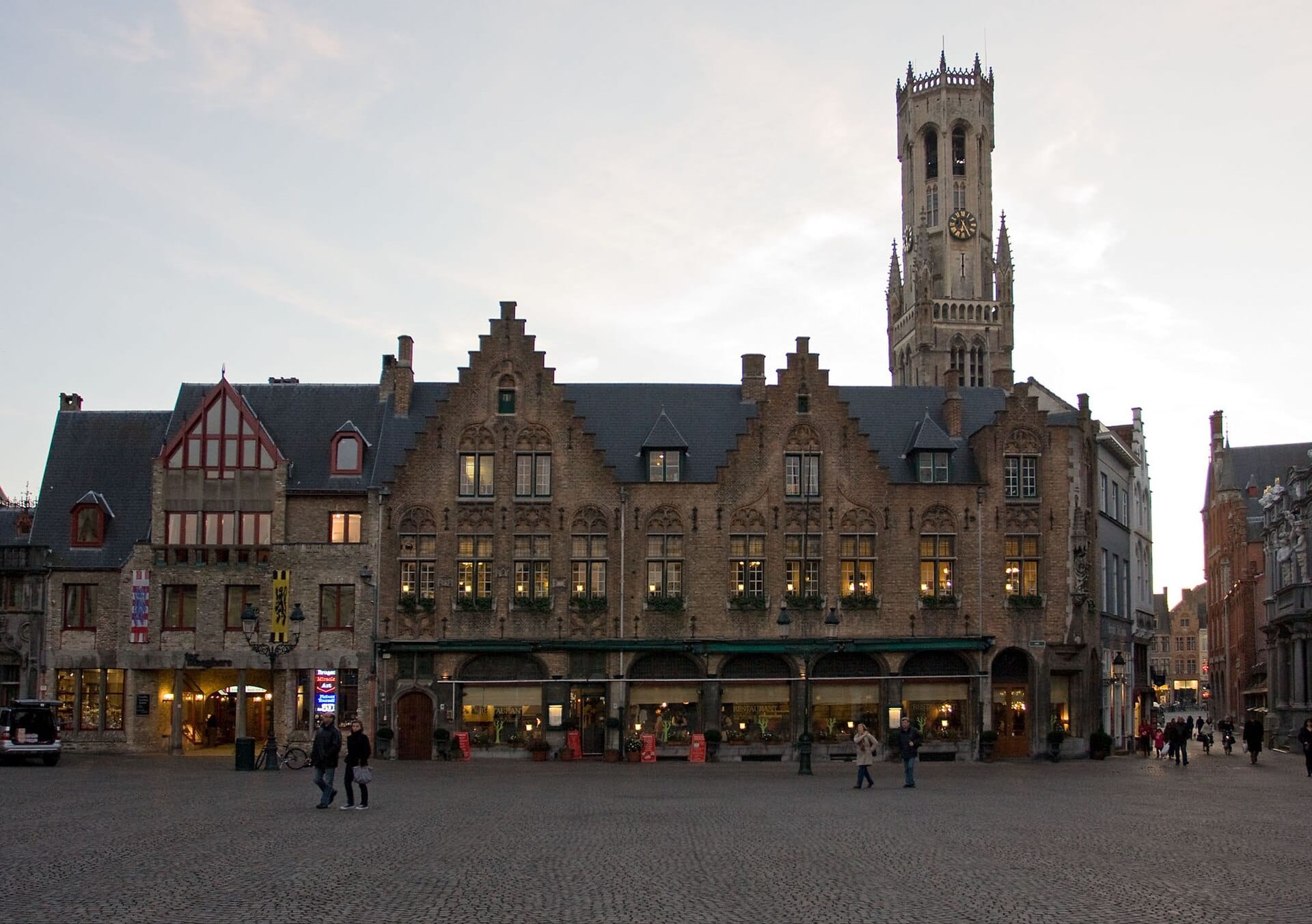 A historic square in central Bruges with step-gabled brick buildings and the Belfort tower behind