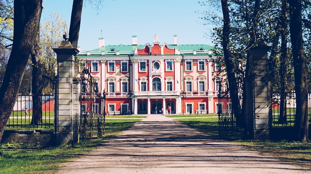 The pink Baroque Kadriorg Palace with a green roof seen through park gates in Tallinn
