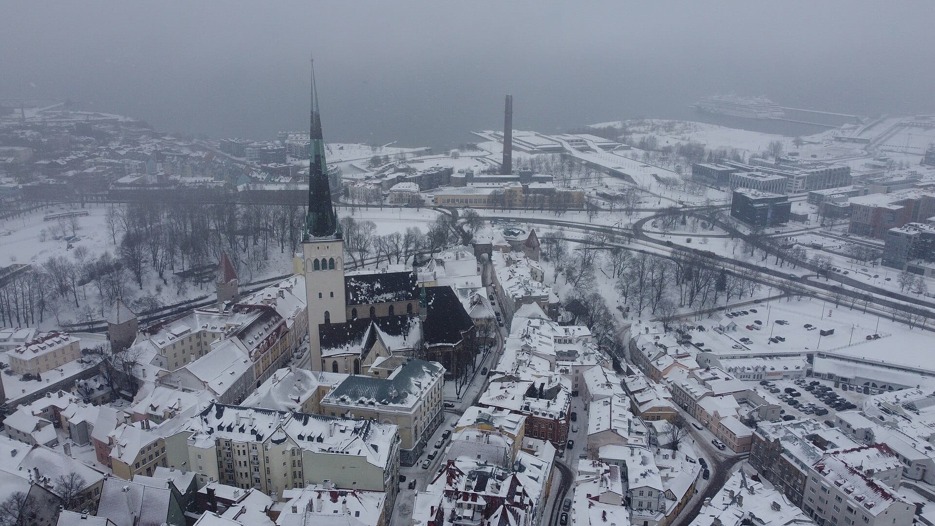 Aerial view of St Olaf's Church and its tall green spire above the snowy rooftops of Tallinn Old Town