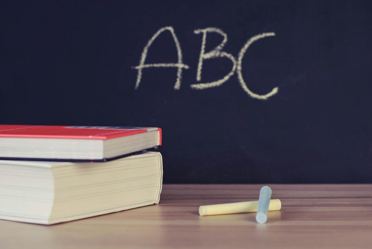 A stack of school books and chalk on a desk with ABC written on a blackboard background, generic Dubai schools illustration