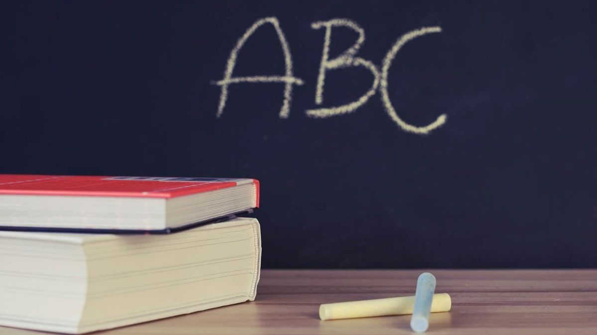 A stack of school books and chalk on a desk with ABC written on a blackboard background, generic Dubai schools illustration