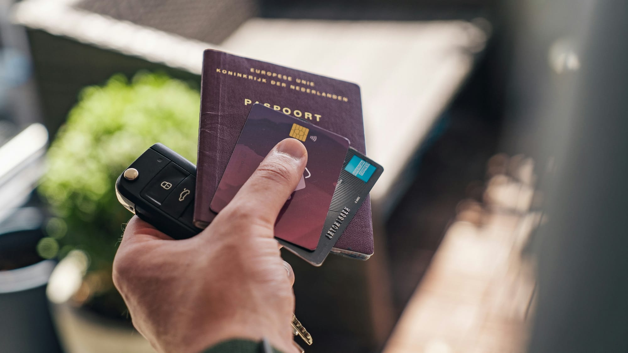 A hand holding a passport, a bank card, and a car key