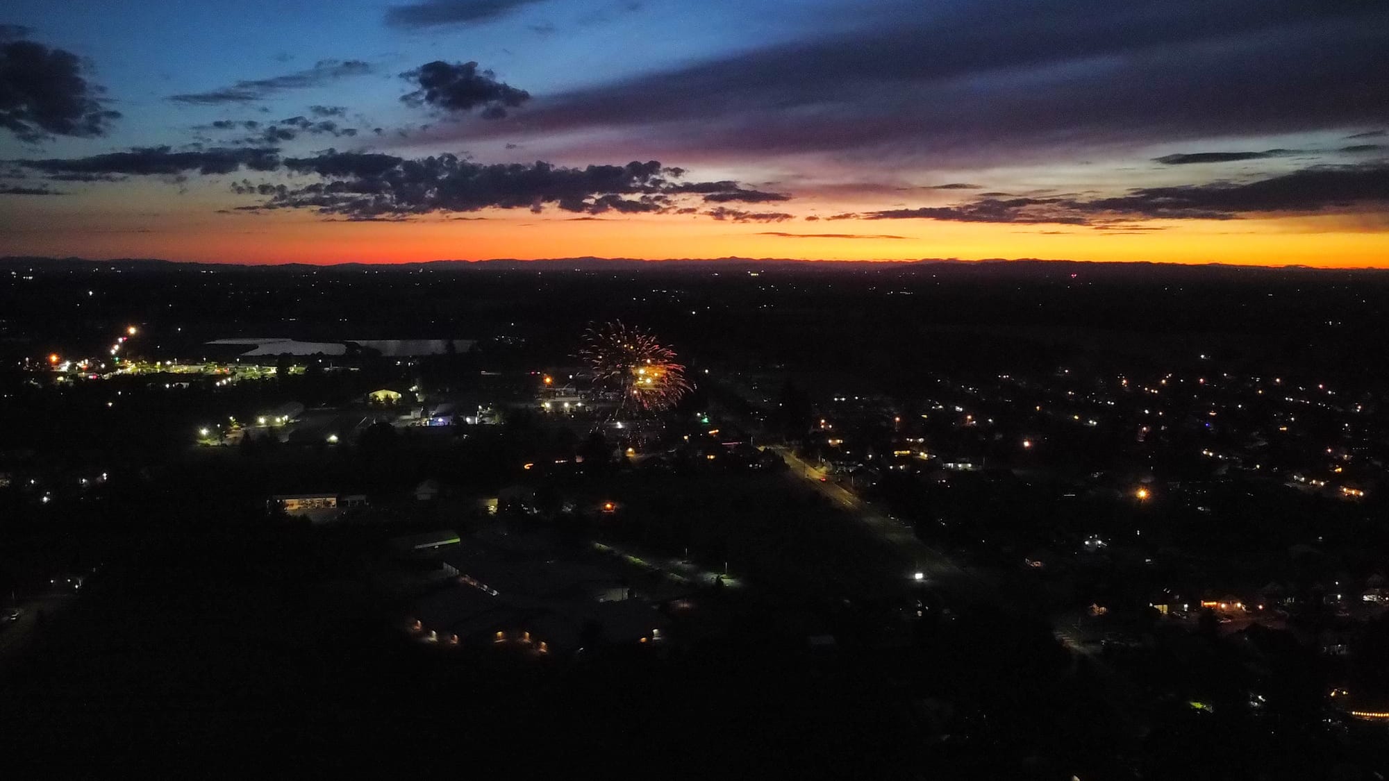 an aerial sunset view of a firework bursting over a darkening town