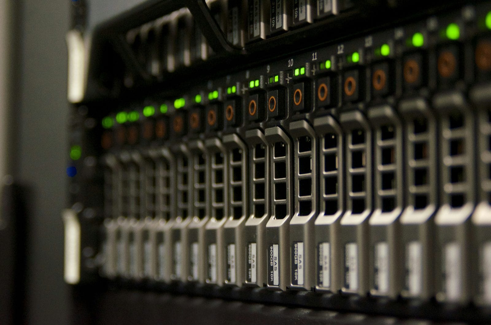 A close-up row of server hard drives with green status lights in a data center.