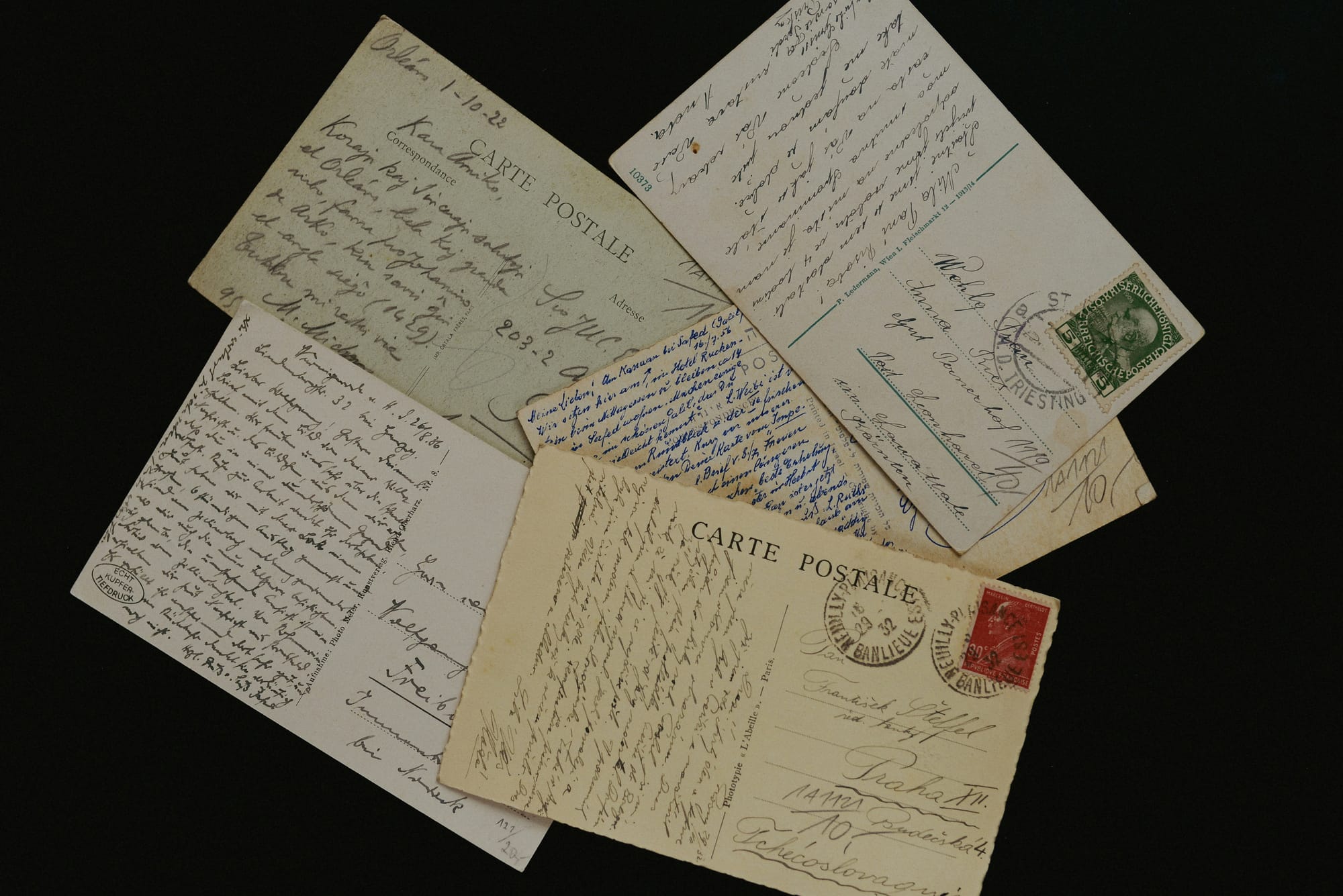 A handful of old handwritten postcards fanned out on a dark surface.