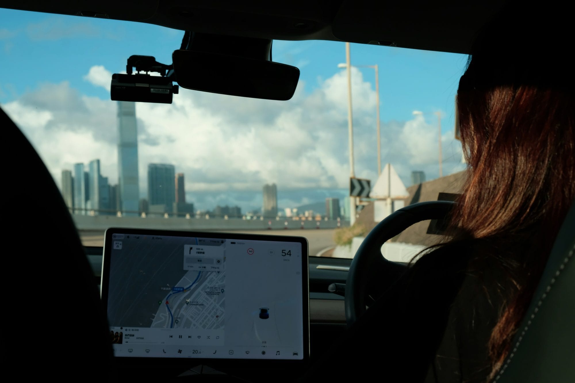 Inside a Tesla, the Full Self-Driving screen on, a driver's hand near the wheel