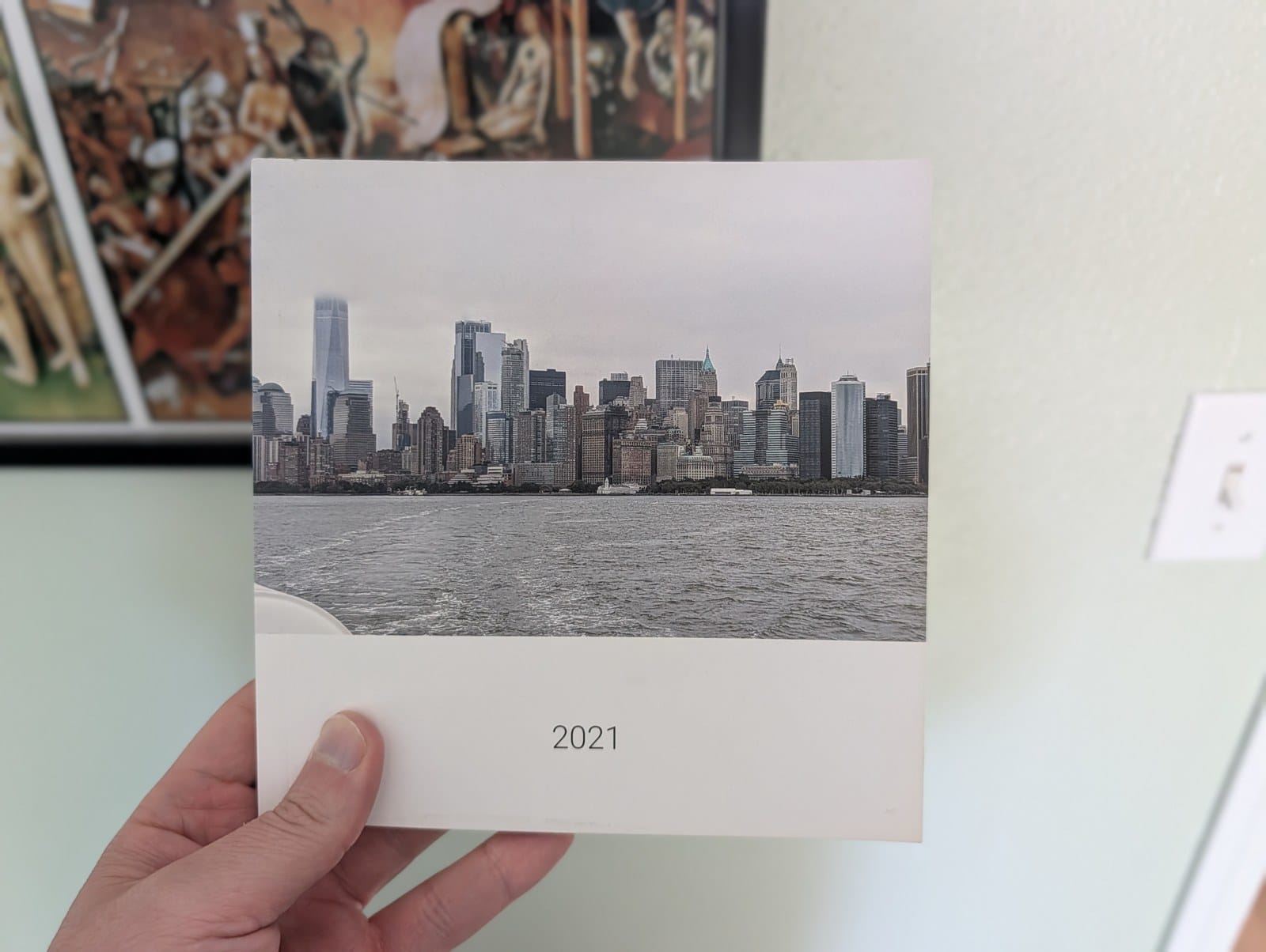A hand holding a softcover Google Photos book with a city skyline cover photo and the title 2021.