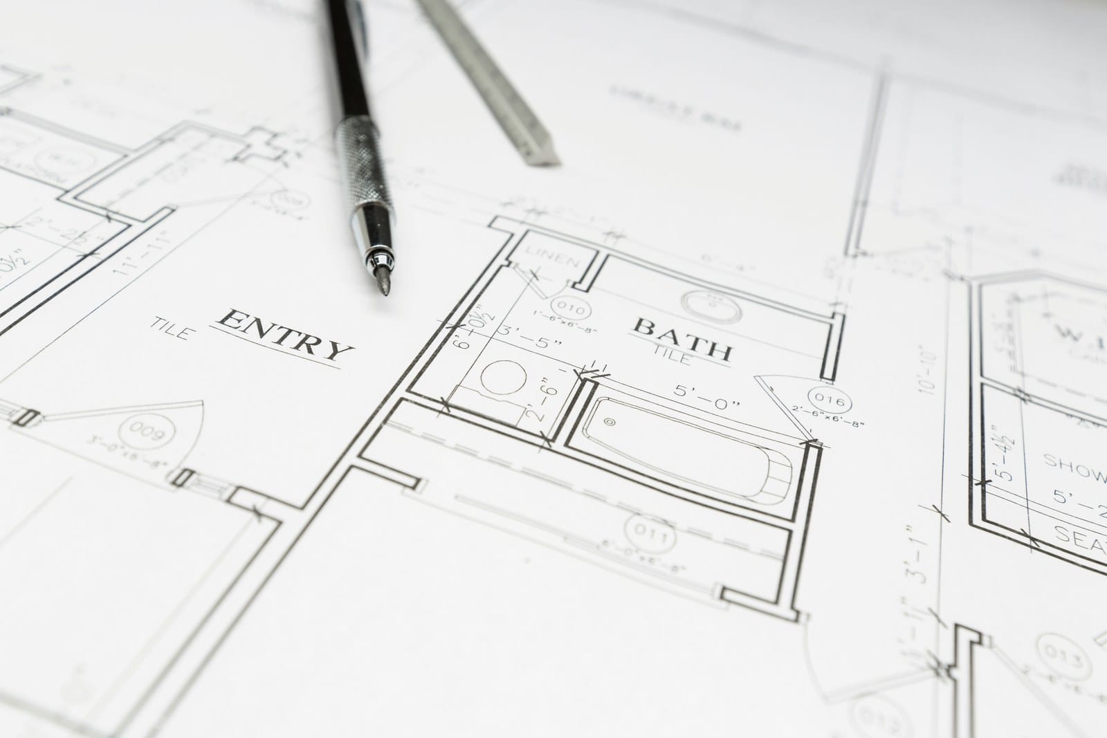 Architectural floor plan drawings with rooms labeled ENTRY and BATH, a drafting pen resting on the paper
