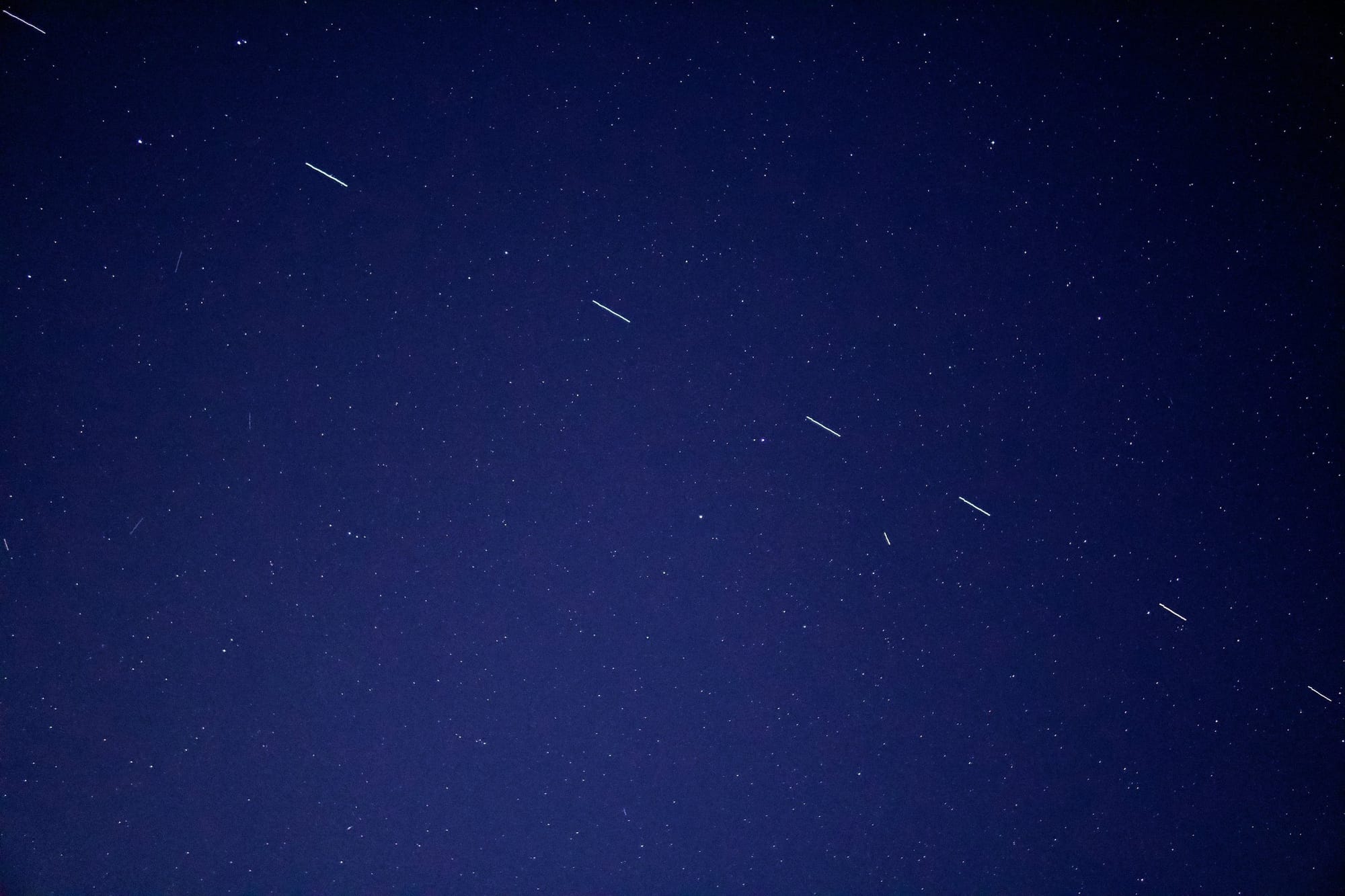 Long-exposure night sky with several short white satellite streaks among the stars.