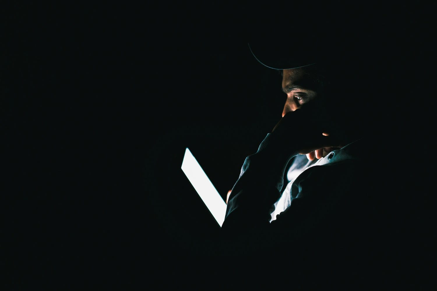 A person's face half-lit by a bright screen in the dark.