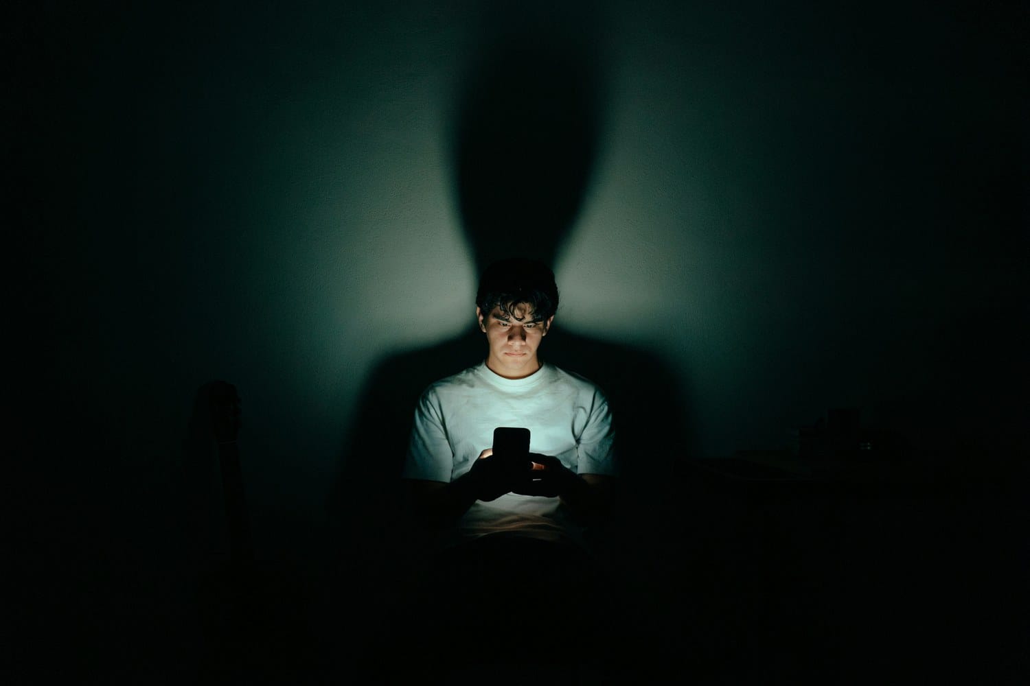 A person in a dark room, face lit by the phone in their hands.
