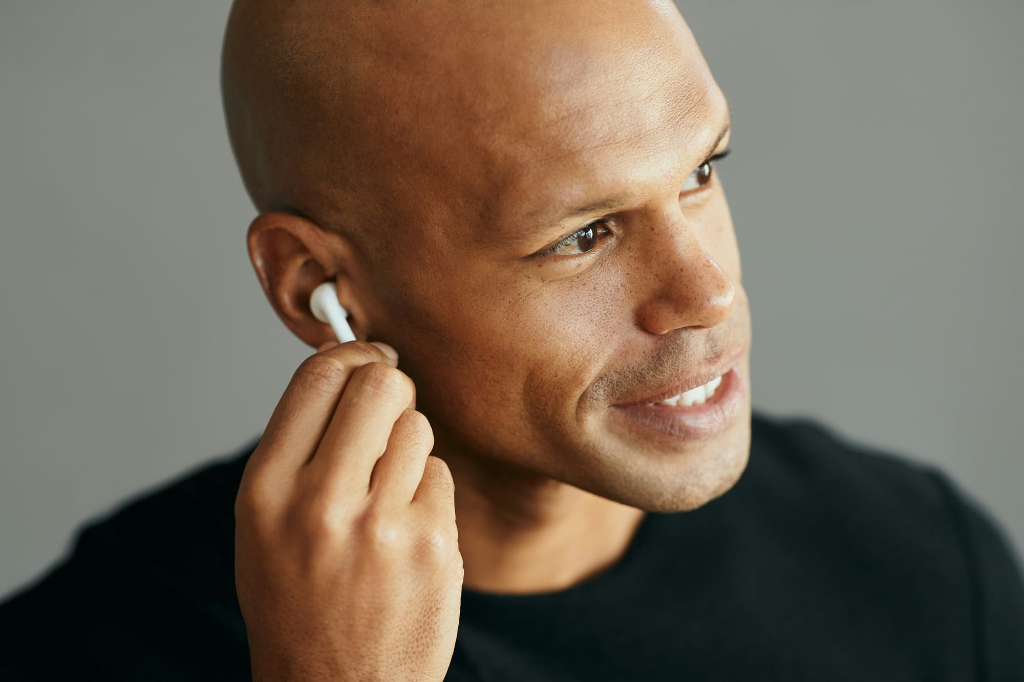 A man placing a white wireless earbud into his ear.