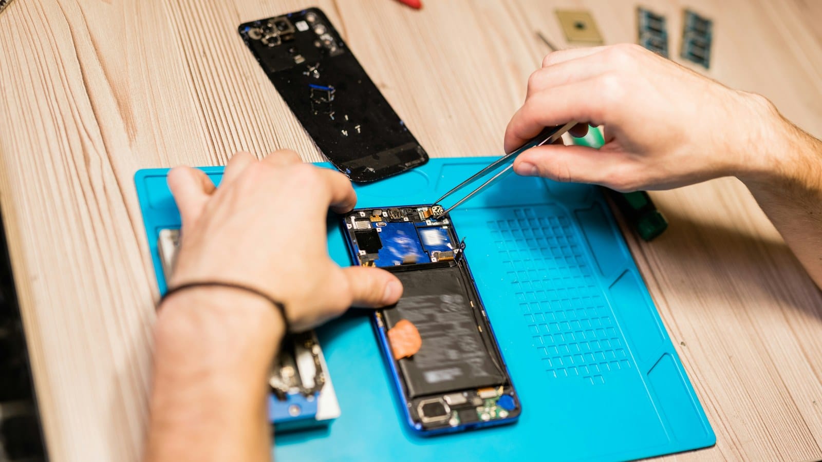 A technician uses tweezers on an opened smartphone with its battery exposed