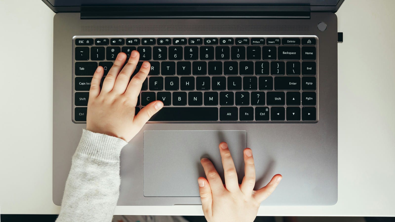 Overhead view of a small child's hands resting on a laptop keyboard and trackpad