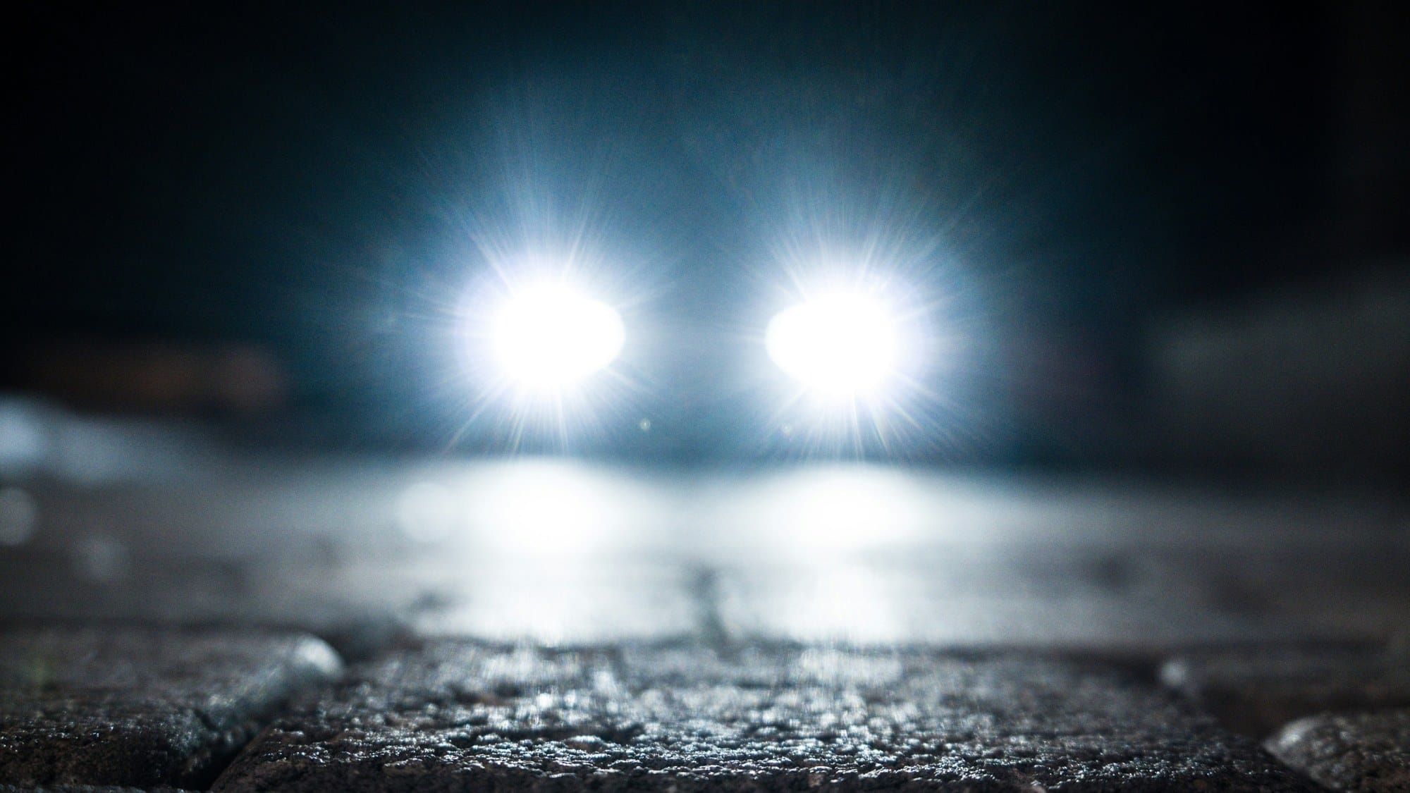 Headlights of an oncoming car on a wet road at night.
