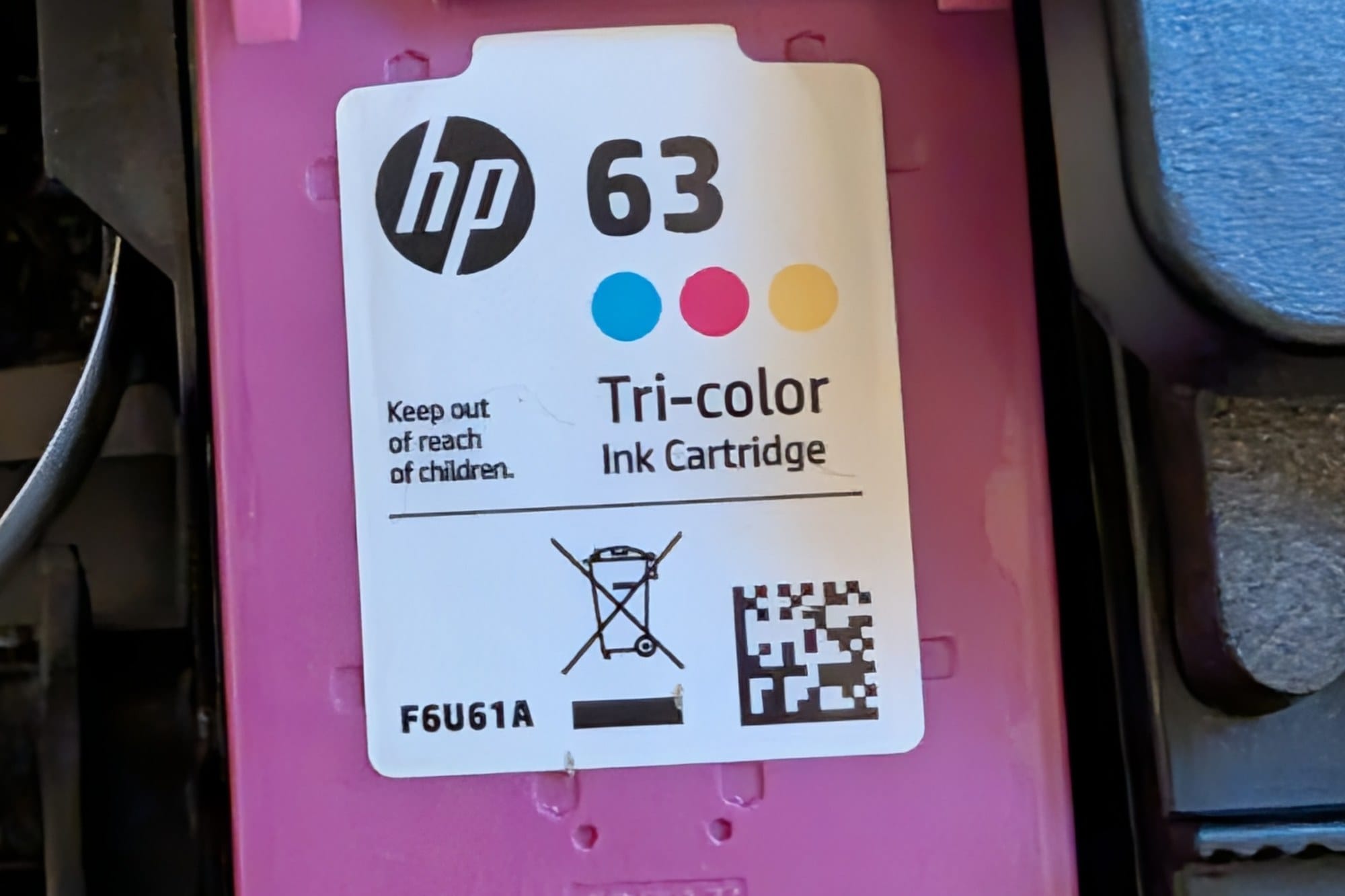 An HP 63 tri-color ink cartridge seated in a printer's magenta cradle, the number 63 printed on its label