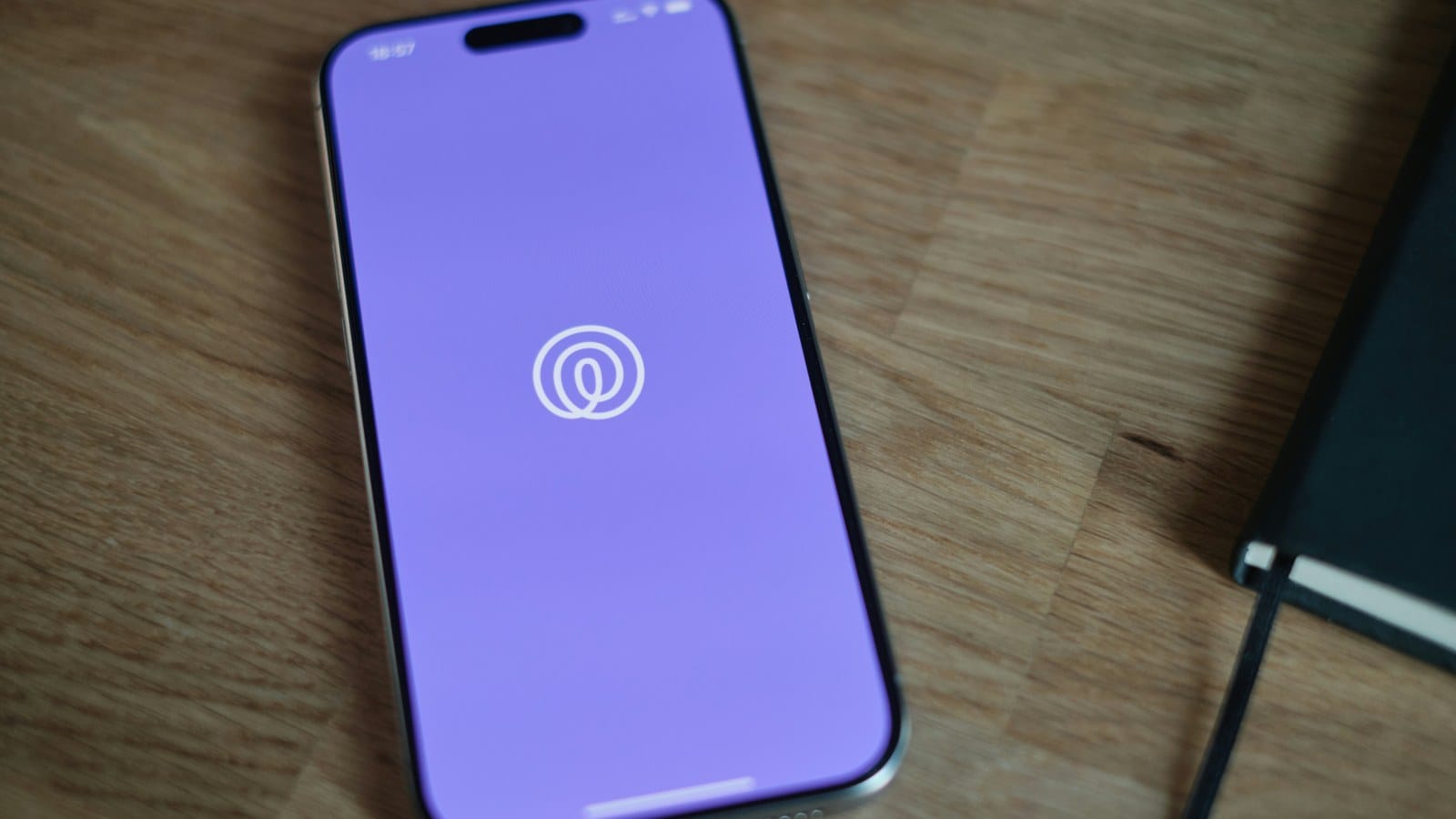 The Life360 app opening on a smartphone lying face up on a wooden desk beside a notebook.