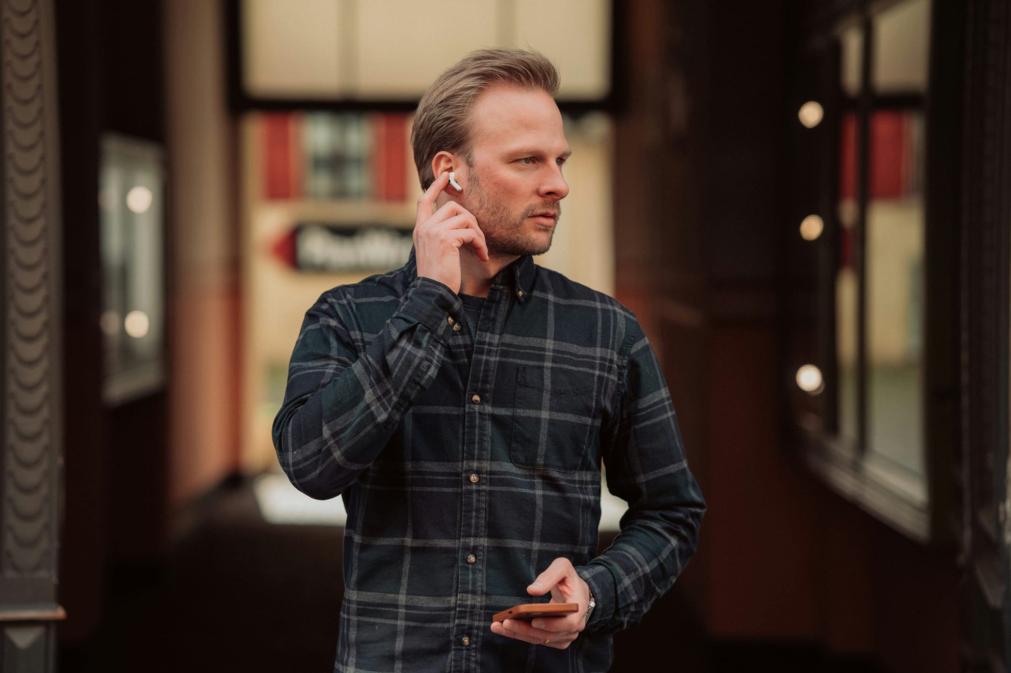 A man on a sidewalk touching the AirPod in his ear while holding his phone.