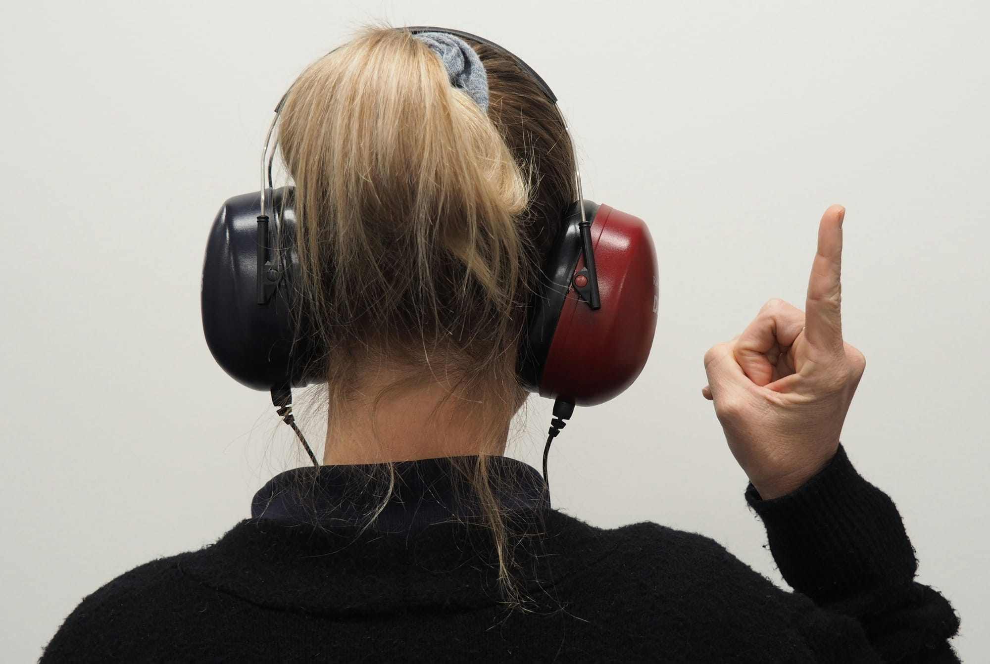 A person seen from behind wearing audiometry headphones and raising one finger during a hearing test.