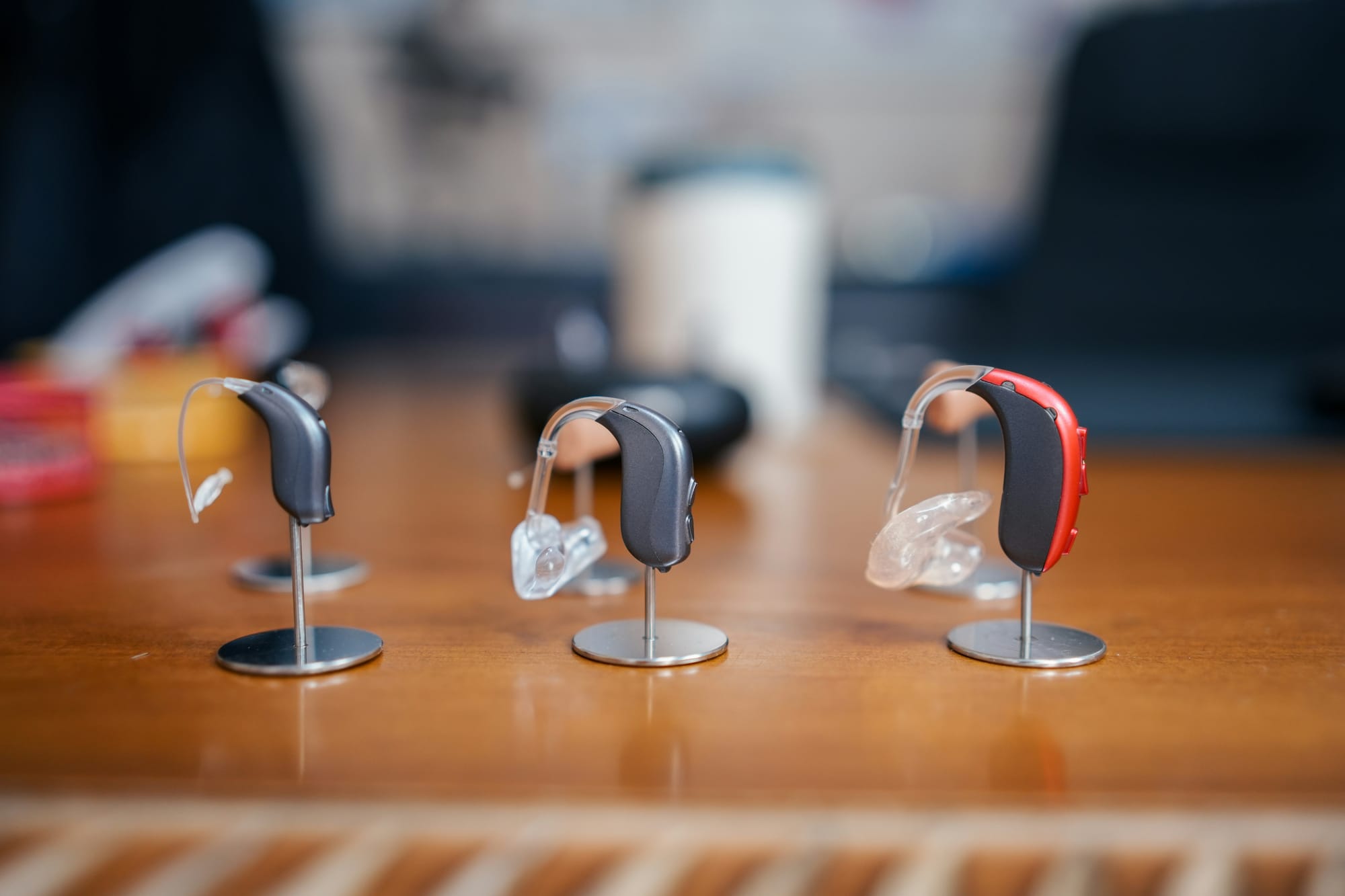 Three behind-the-ear hearing aids displayed on small metal stands on a wooden table.