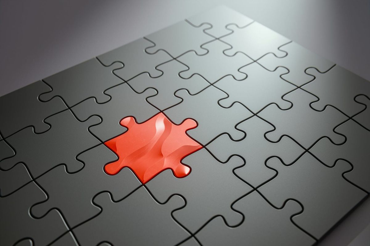 A grid of gray jigsaw puzzle pieces with one orange piece standing out.
