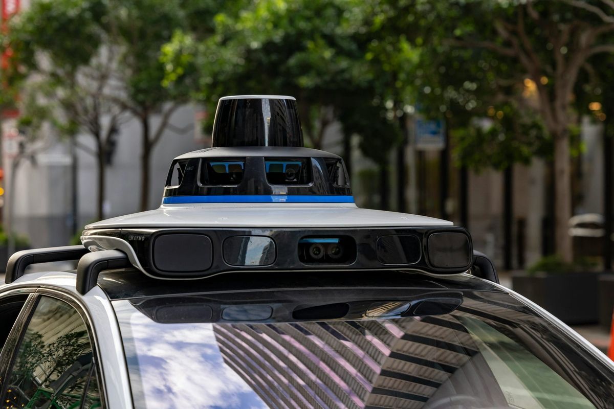 Close-up of a robotaxi's roof-mounted lidar and camera sensor array on a city street