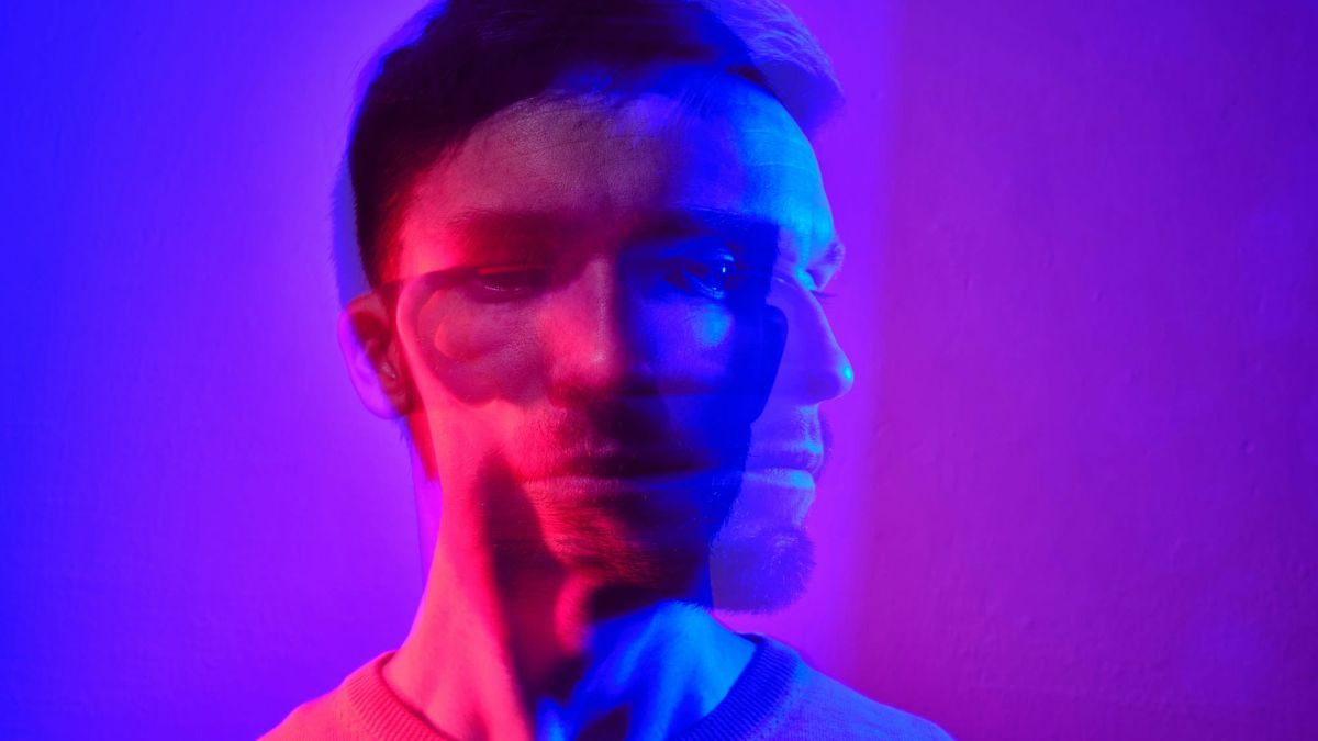 Double exposure portrait of a man lit in red and blue, his face overlapping a second ghosted copy of itself