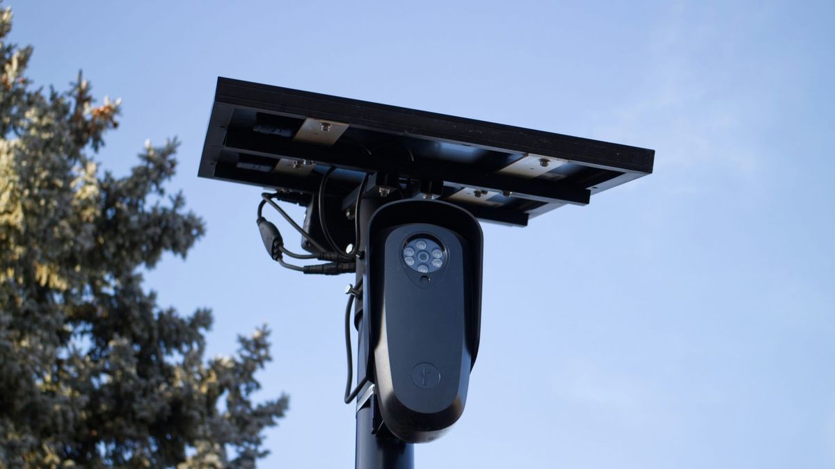 A pole-mounted automatic license plate reader with a small solar panel, against a blue sky