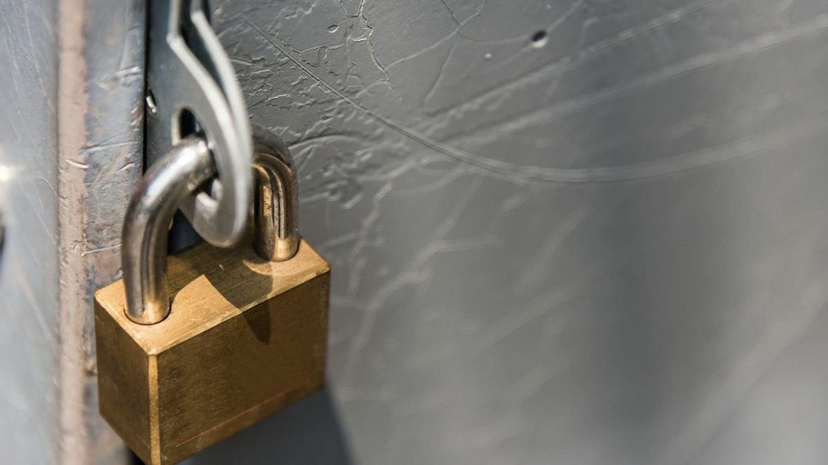 A closed brass padlock on a gray metal door.