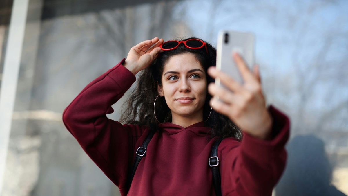 A woman holding up her phone to record a selfie video of her own face outdoors