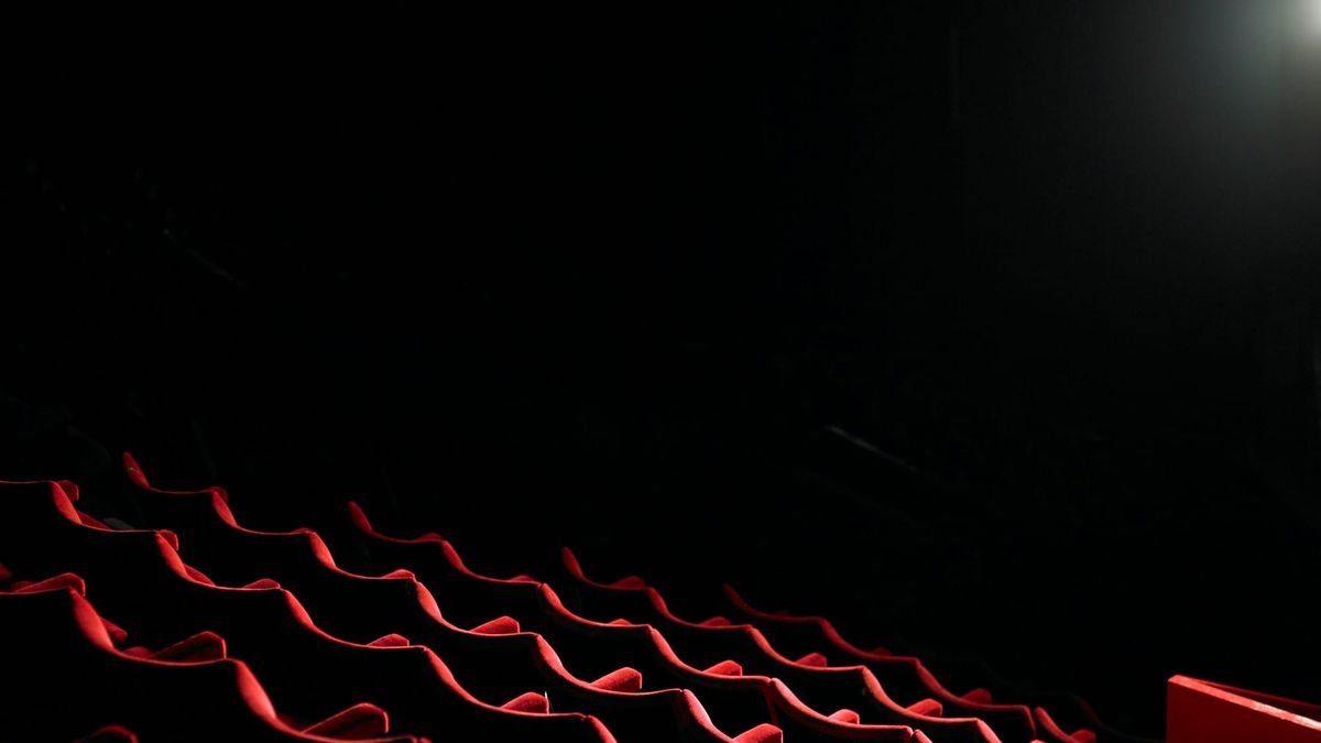 Rows of empty red seats in a dark movie theater, lit by a single projector beam