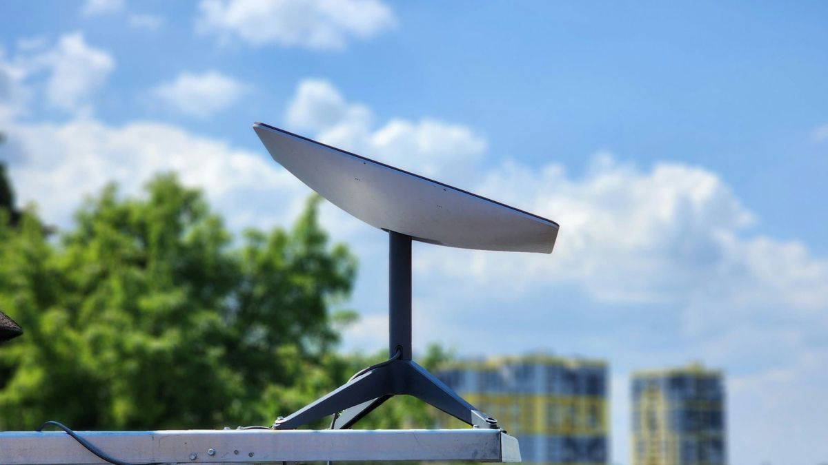 A Starlink satellite dish on a metal mount against a blue sky, with trees behind it.