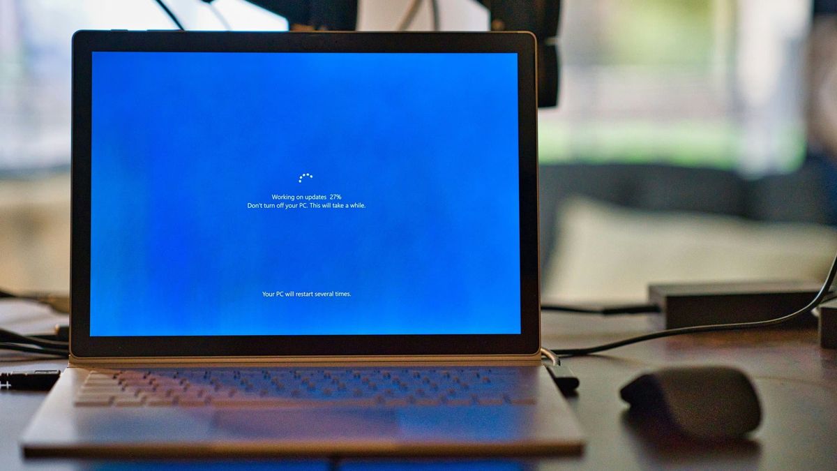 A laptop on a desk showing the blue Windows update screen: “Working on updates 27%. Don’t turn off your PC.”