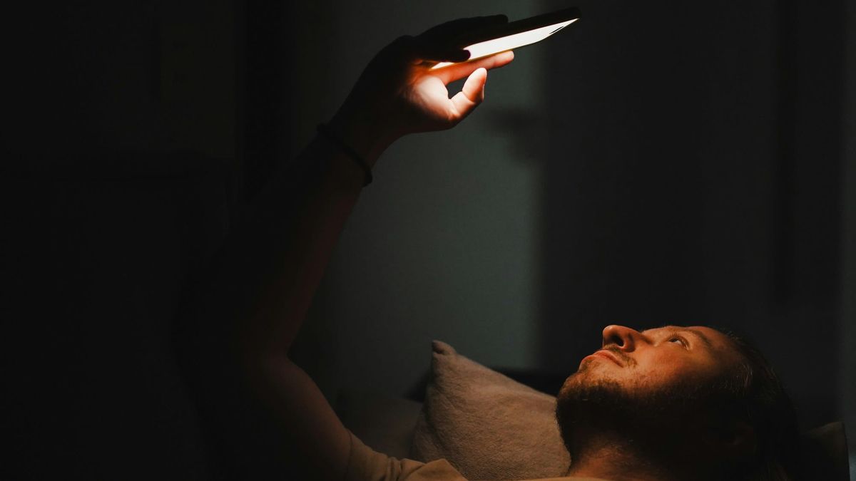 A person lying in the dark, face lit by the glow of a smartphone.