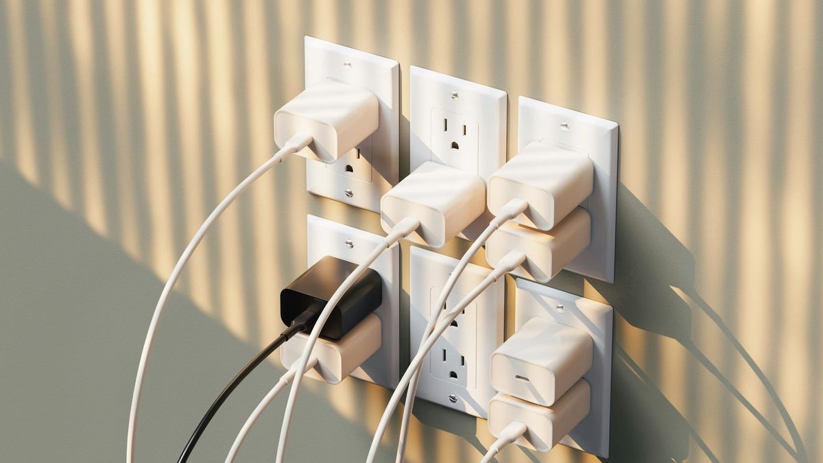 A bank of wall outlets crowded with white phone chargers, lit by afternoon sun through blinds