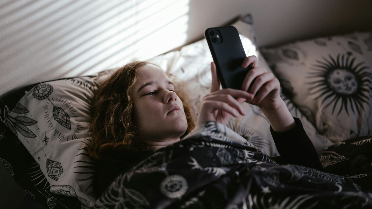 A teenage girl lies on her bed in her own room, absorbed in her phone.