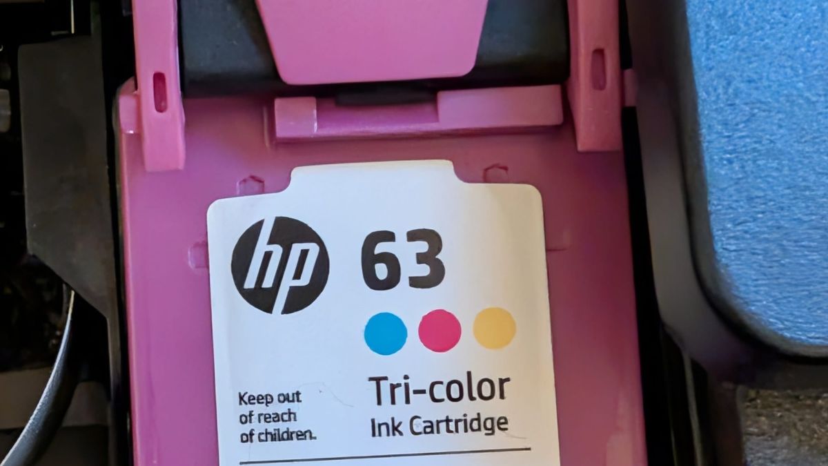 An HP 63 tri-color ink cartridge in a printer's magenta cradle, the number 63 printed on its label