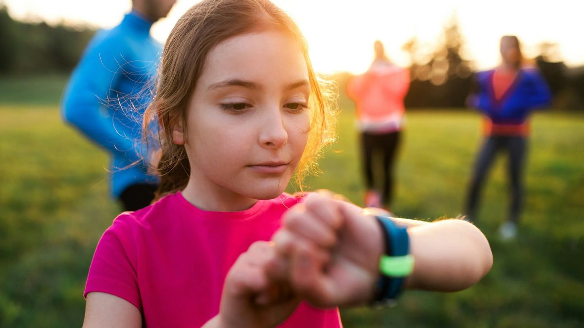 A girl in a pink shirt checking the smartwatch on her wrist in a field at sunset