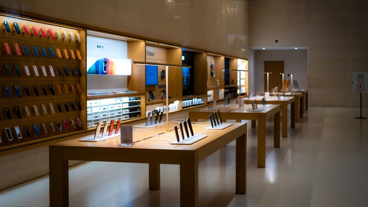 iPhones on display stands beside a small price card on a wooden table in an electronics store