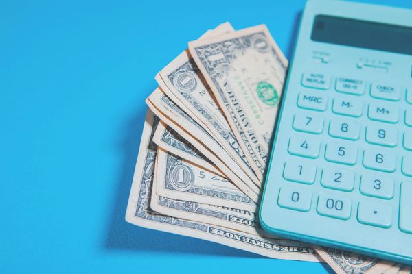 A teal calculator beside a fan of US one-dollar bills on a blue background.